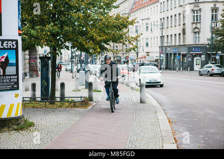 Ein älterer Mann auf einem Roller reitet eine spezielle Radweg entlang der Straße der Stadt neben den Gebäuden, Straßen, Autos. Umweltfreundliche Verkehrsmittel ar Stockfoto