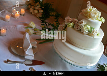 Gedeckter Tisch miteinem weisse Hochzeitstorte mit vielen Pfirsich und weißen Rosen auf der Oberseite, Tisch hatte Rosen und Kerzen Stockfoto