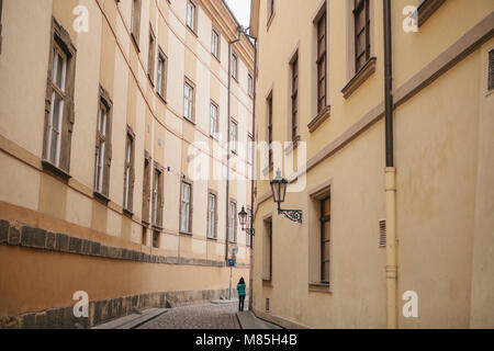 Unbekannte touristische Mädchen in der grünen Jacke Spaziergänge entlang der wunderschönen einsamen Gasse in Prag zwischen zwei historischen Gebäuden Stockfoto