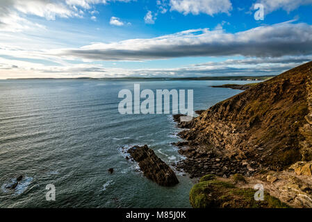 Einen malerischen Blick auf die Felsen in alten Kopf von Kinsale Halbinsel in Irland mit grünen Hügeln bei Sonnenuntergang. Stockfoto