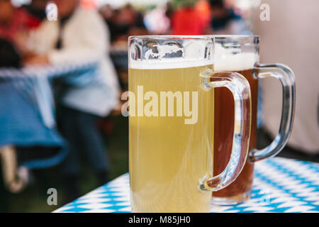 Die Feier der traditionellen deutschen Bier Festival namens Oktoberfest. Zwei Becher mit einem hellen und dunklen Bier stand auf dem Tisch. Im Hintergrund, blurre Stockfoto