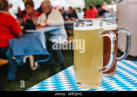 Die Feier der traditionellen deutschen Bier Festival namens Oktoberfest. Zwei Becher mit einem hellen und dunklen Bier stand auf dem Tisch. Im Hintergrund, blurre Stockfoto