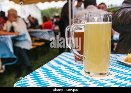 Die Feier der traditionellen deutschen Bier Festival namens Oktoberfest. Zwei Becher mit einem hellen und dunklen Bier stand auf dem Tisch. Im Hintergrund, blurre Stockfoto