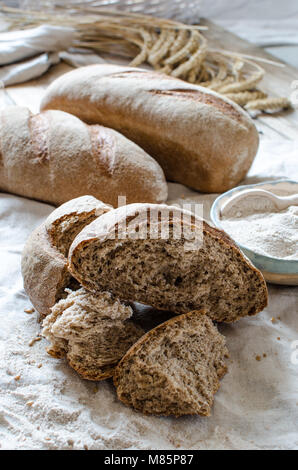 Vollkornbrot und Mehl auf hellen Hintergrund. Keramische Schüssel voller Vollkornmehl Stockfoto