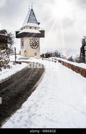 Sun flares über verschneite Uhrturm Uhrturm Wahrzeichen auf Berg Schlossberg mit Luftaufnahme der Stadt Graz im Winter Stockfoto