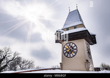 Sun flares über verschneite Uhrturm Uhrturm Wahrzeichen der Stadt Graz auf Hill Schlossberg im Winter Stockfoto