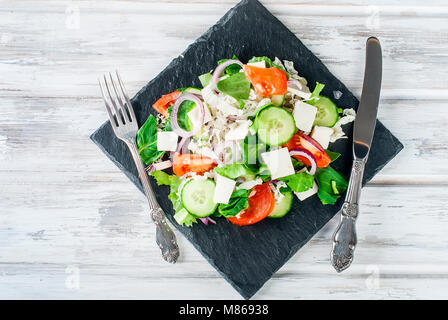 Ein gemischter Salat mit Gurken, Tomaten, Käse, Spinat und rote Zwiebel auf blak Platte/gesundes Essen. Ansicht von oben. Kopieren Sie Platz. Stockfoto