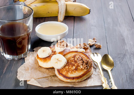 Hausgemachte Pfannkuchen mit Banane, Nüsse, Honig und Tasse Kaffee auf dunklem Hintergrund, Frühstück einstellen. Kopieren Sie Platz Stockfoto