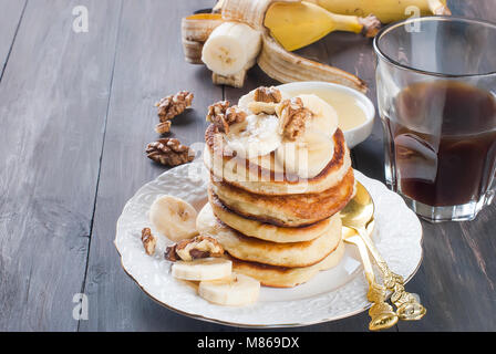 Hausgemachte Pfannkuchen mit Banane, Nüsse, Honig und Tasse Kaffee auf dunklem Hintergrund, Frühstück einstellen. Kopieren Sie Platz Stockfoto