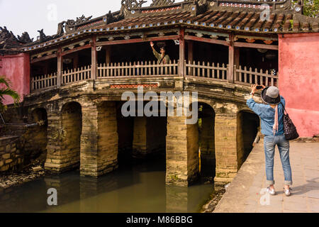 Eine Frau nimmt ein Foto von ihrem Mann auf dem Chùa Cầu japanische Brücke, aus dem 18. Jahrhundert geschnitzte hölzerne Brücke, der einen Schrein, in Hoi An, Vietnam Stockfoto