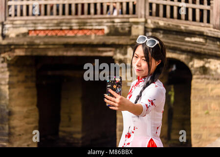 Eine Frau nimmt eine selfie Chùa Cầu an die japanische Brücke, eine hölzerne Brücke aus dem 18. Jahrhundert, der einen Schrein, in Hoi An, Vietnam geschnitzt Stockfoto