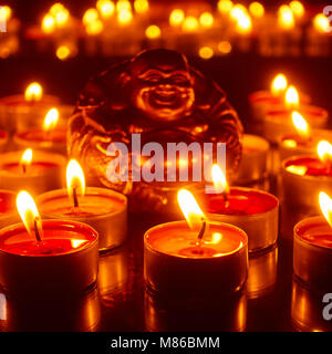 Brennende Kerzen und Figürchen von Lucky Buddha. Konzentrieren Sie sich auf die vorderen Kerzen Stockfoto