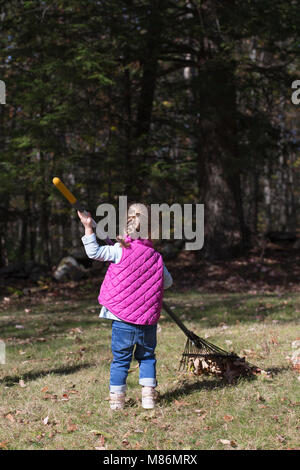 Kleinkind Mädchen lernen Blätter an einem kühlen Herbsttag in Maine zu rechen Stockfoto