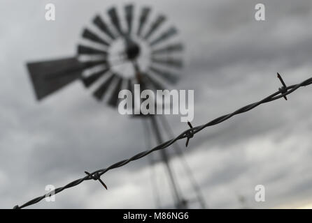 Eine altmodische Mühle steht hinter einem Stacheldraht zaun entlang einer ländlichen Strecke der alten Route 66 im Südwesten der Vereinigten Staaten. Stockfoto