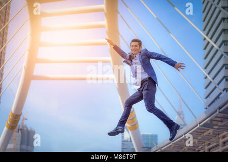 Portrait von Business Mann springen mit Arme feiern auf unscharfen Stadt Hintergrund. Geschäftlicher Erfolg Konzept Stockfoto