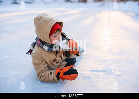 Junge lag auf einem zugefrorenen See mit Schlittschuhen Eis essen Stockfoto