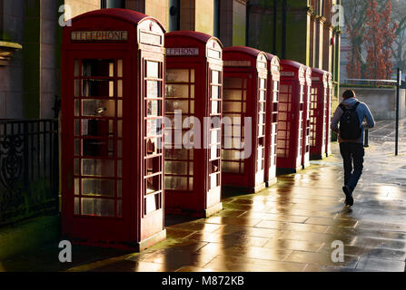 Junger Mann vorbei gehen acht roten Telefonzellen, am frühen Morgen, Preston, Lancashire, Großbritannien. Stockfoto