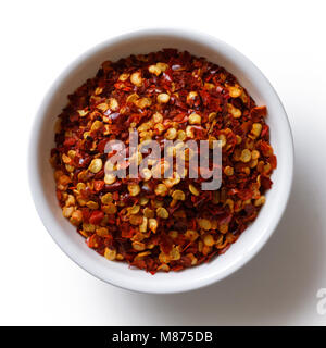 Grob Gemahlenes Chili peppers aus weisser Keramik Schüssel auf Weiße von oben isoliert. Stockfoto