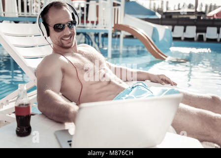 Strahlende Geschäftsmanns, der auf dem Laptop beim Sonnenbaden Stockfoto