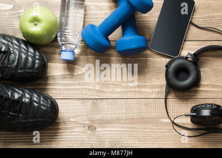 Sport und Fitness Ausrüstung mit Sneakers, Hanteln, Handtuch und Kopfhörer auf Holzbrett. Ansicht von oben mit Platz für Ihren Text. Stockfoto