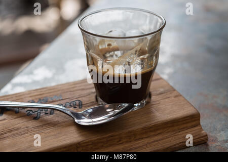 Ein doppelter Espresso Kaffee in einem Glas auf einem Holzbrett mit Löffel serviert. Stockfoto