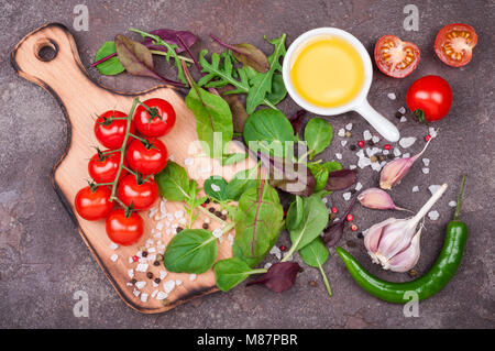 Frisches Bio-Gemüse, Olivenöl, Kräutern und Gewürzen. Gemischter Salat, Tomaten, Chili und Knoblauch auf Stein Hintergrund. Gesunde Ernährung, gesunder Lebensstil und Stockfoto