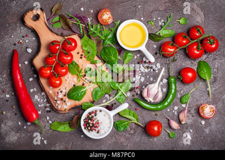 Frisches Bio-Gemüse, Olivenöl, Kräutern und Gewürzen. Gemischter Salat, Tomaten, Chili und Knoblauch auf Stein Hintergrund. Gesunde Ernährung, gesunder Lebensstil und Stockfoto