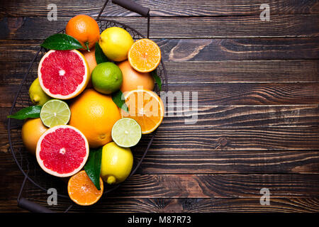 Frische Zitrusfrüchte in Korb. Orange, Grapefruit, Zitrone, Limette, Mandarine auf dunklen Holztisch. Verschiedene frische Zitrusfrüchte mit Blättern. Ansicht von oben und Stockfoto