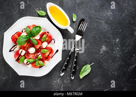 Caprese Salat. Tomaten, Mozzarella, Tomaten, Olivenöl, Basilikum Kräuter verlässt, Balsamico Sauce auf dunklem Hintergrund. Italienisches Essen. Ansicht von oben Stockfoto