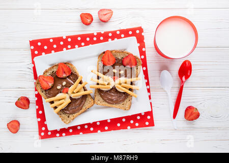 Sandwiches und Milch für die Kinder. Lustige Katzen Gesicht Sandwiches mit Beeren, Schokolade, Bananen, Nüsse. Ansicht von oben Stockfoto