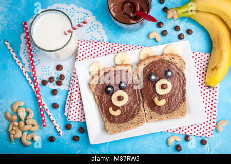 Kinder Frühstück mit Brötchen und Milch. Lustige bärengesicht Sandwiches mit Schokoladencreme, Bananen, Nüsse und Beeren. Ansicht von oben Stockfoto