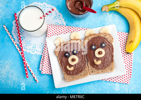 Kinder Frühstück mit Toast und Milch. Lustige bärengesicht Sandwiches mit Schokoladencreme, Bananen, Nüsse und Beeren. Ansicht von oben Stockfoto