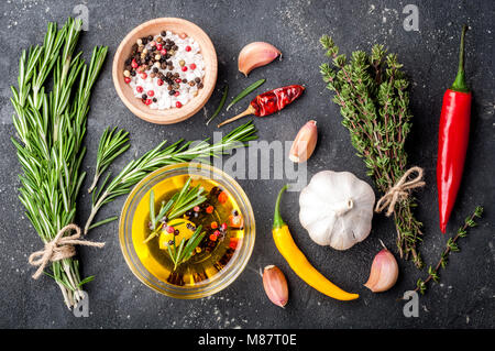 Kräuter und Gewürze. Rosmarin, Thymian, Chili, Knoblauch, Olivenöl, Salz und Pfeffer auf dunklen Tisch. Zutaten zum Kochen. Ansicht von oben Stockfoto