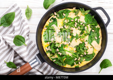 Spinat tortilla in der Pan auf weißem Hintergrund. Omelette mit Eier, Spinat, Pinienkernen und Gemüse. Köstliches Frühstück Vorspeise oder Snack. Ansicht von oben Stockfoto