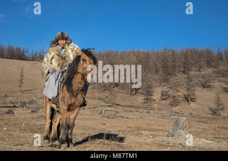 Mongolische Mann mit einem Wolf haut Jacke, reiten sein Pferd in einer Steppe im Norden der Mongolei Stockfoto