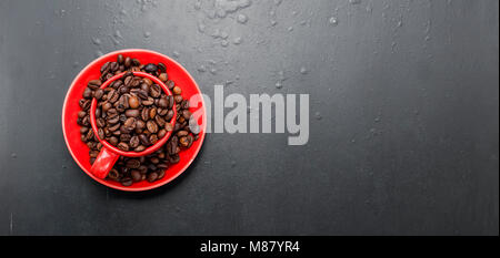 Rote Schale und Kaffeebohnen auf schwarzem Hintergrund, Ansicht von oben, kopieren Raum Stockfoto