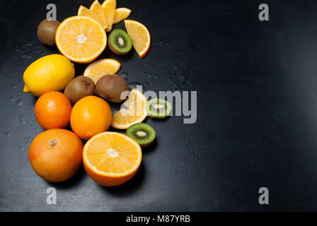 Vielzahl von frischen Zitrusfrüchten auf dunklem Hintergrund aus Schichten von Kiwi und Orangen, kopieren Raum Stockfoto