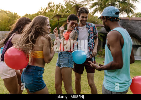 Gruppe von Frauen und Männern spielen Ballon platzen Spiel während einer Partei. Freunde genießen, spielen sie bei der Party im Freien. Stockfoto