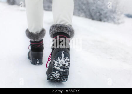 Detail der Frau, die ihre schwarzen und grauen Schnee boot Heben mit Fellimitat und violetten Spitzen, die Lauffläche der Stiefel, Winter bewölkten Tag erschossen. Stockfoto