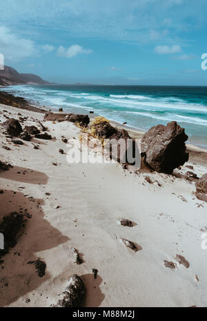 Riesige vulkanischen Stein Boulder auf spektakulären weißen Sanddünen von entfernten menschenleeren Strand Praia Grande. Ocean schlagen Küste im Hintergrund. Karge Vegetation. Calhau, Sao Vicente Kapverden Stockfoto