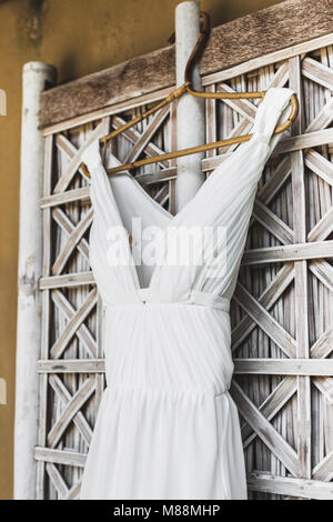 Lange weiße Hochzeit Kleid hängen außerhalb der traditionellen Bali Haus auf Fenster mit weissen Korbmöbeln Fensterläden Stockfoto