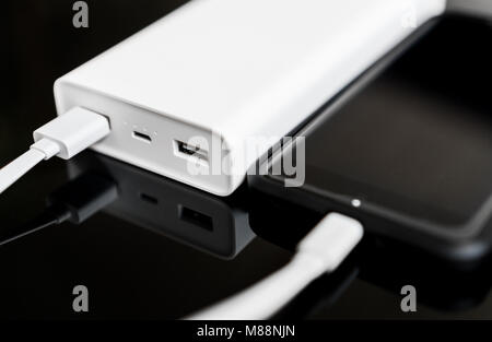 White Power Bank mit Smartphone auf verspiegelte Oberfläche. Stockfoto