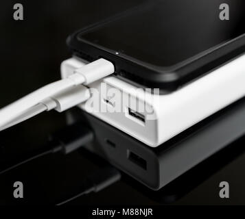 White Power Bank mit Smartphone auf verspiegelte Oberfläche. Stockfoto