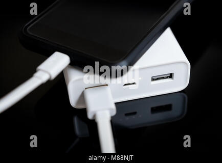 White Power Bank mit Smartphone auf verspiegelte Oberfläche. Stockfoto