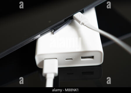 White Power Bank mit Smartphone auf verspiegelte Oberfläche. Stockfoto