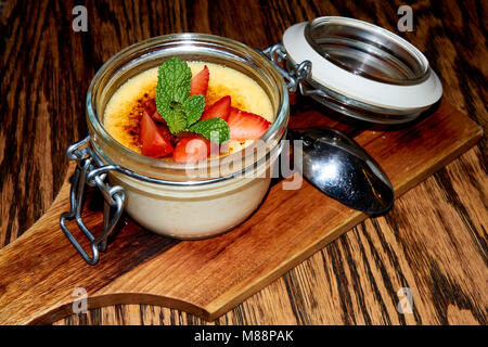 Creme brulle Dessert im Glas und Metall Glas mit einer Erdbeere und Minze Topping auf den dunkelbraunen hölzernen Tisch Hintergrund Stockfoto
