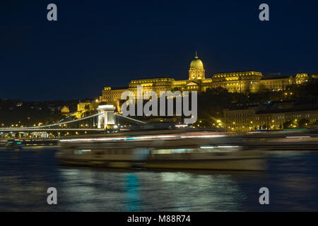 Statische twilight Shot der Budapester Burg und Chain Bridge bei Nacht leuchtet wie ein Boot geht Stockfoto