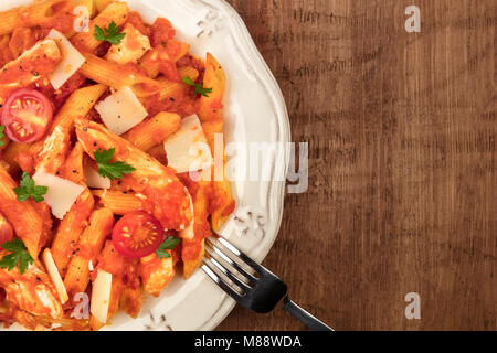 Eine Nahaufnahme von einem Teller Pasta mit Tomatensauce, Hühnchen und Käse. Penne Rigate mit Cherry Tomaten und frische Petersilie, auf einem Stockfoto