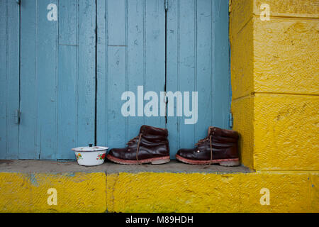 Paar braune Leder Stiefel stehen am Hang eines gelbe Wand vor dem Hintergrund eines blauen geschlossenen Fensterläden aus Holz, moderne Inneneinrichtung Dez Stockfoto