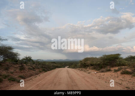 Clay Country Road in der Euphotischen Savannah: der Weg erstreckt sich inmitten der grünen Vegetation, die Berge im Hintergrund reicht, im Süden Äthiopiens. Stockfoto